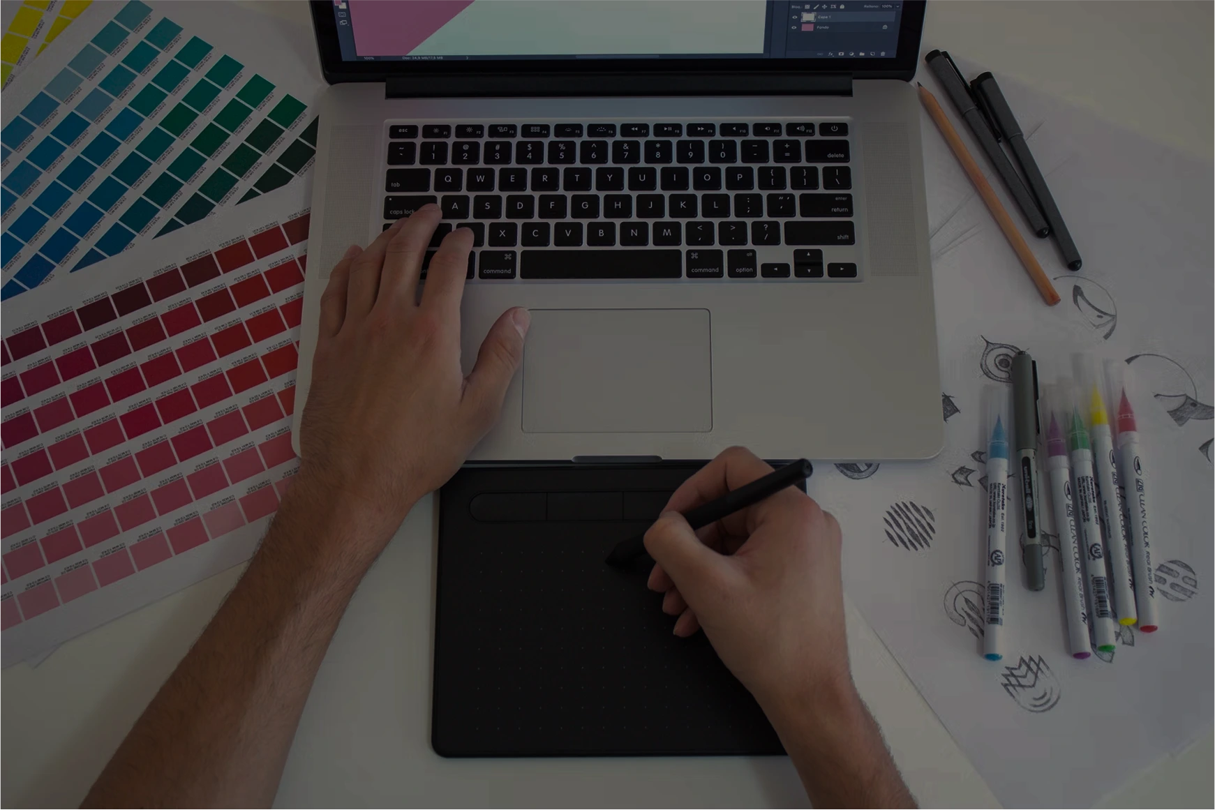 A person drawing on a drawing tablet connected to a laptop, surrounded by paper sketches.